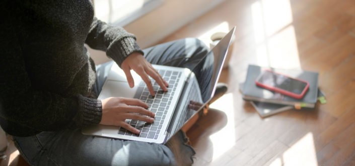 Cropped person sitting on the floor while using the laptop