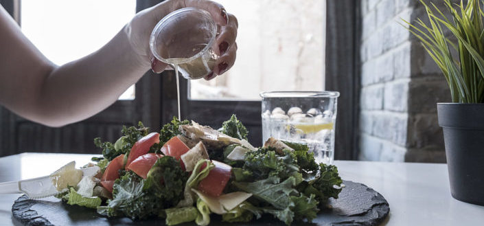 Cropped person putting a dressing on a salad